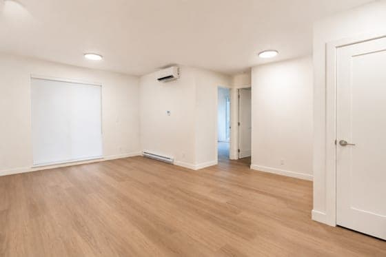 An empty open living and dining area with a roller shade and a hallway